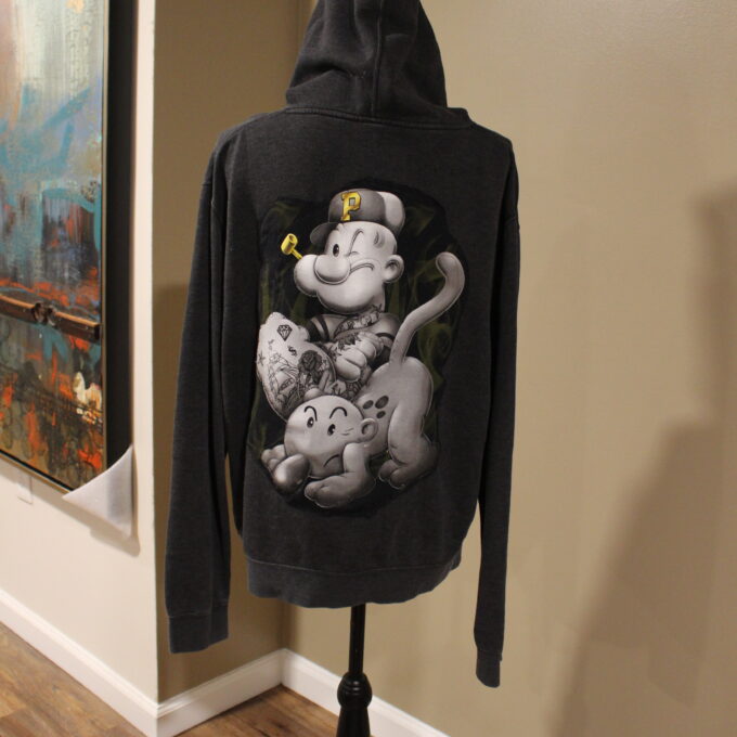 A hoodie with a cartoon character design displayed on a mannequin stand against an indoor background with wall art.