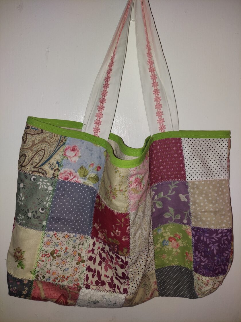 Colorful patchwork tote bag hanging on a white wall, featuring an assortment of floral and polka dot patterns.