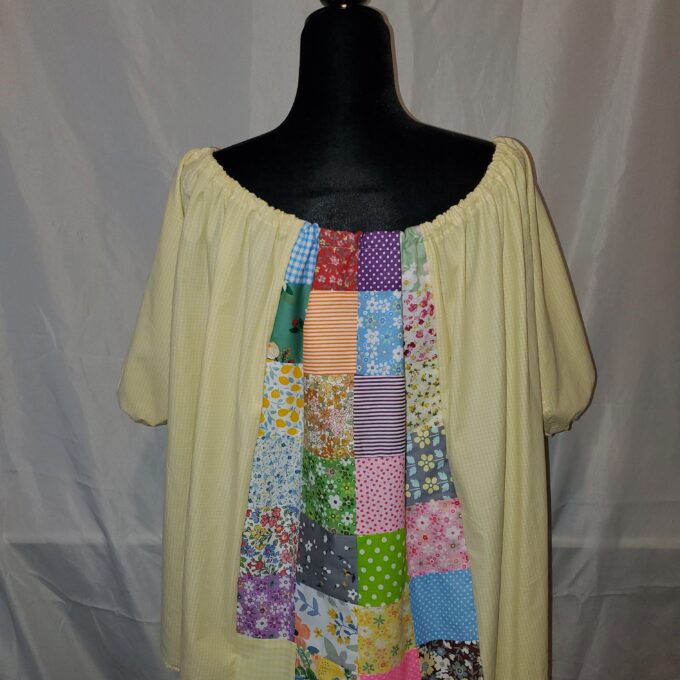 A mannequin displaying a yellow blouse with a colorful patchwork design down the center, set against a white background.