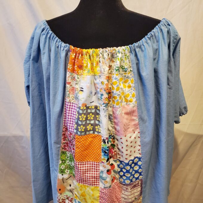 A mannequin displaying a blue off-shoulder blouse with a colorful patchwork design on the front.