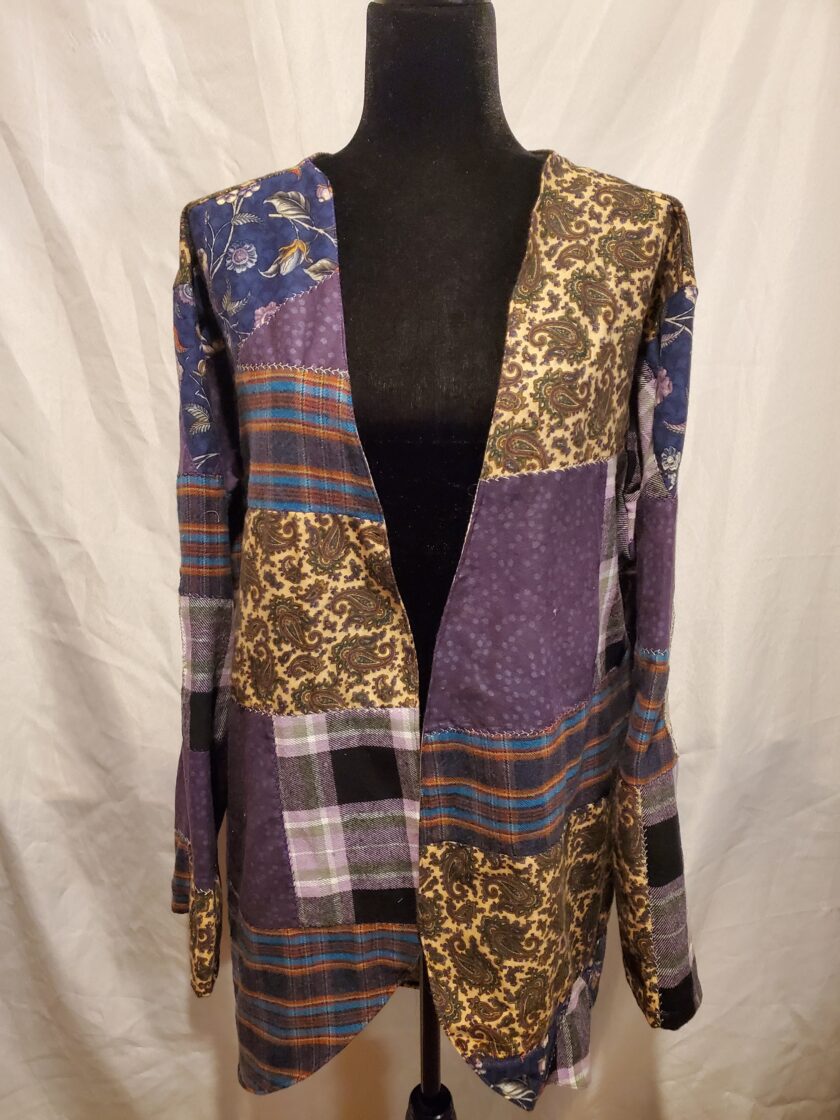 A patchwork cardigan with varying patterns including plaid and floral, displayed on a black mannequin against a white background.