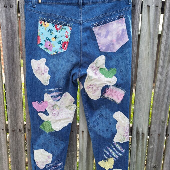 A pair of blue jeans with various floral and patterned fabric patches hanging on a clothesline outdoors.