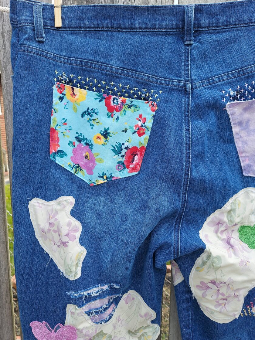 Blue jeans with colorful floral patches hanging on a line, displaying a creative and customized appearance.