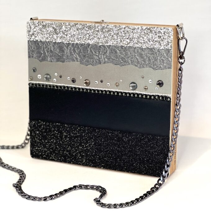 Elegant women's handbag with a striped design, featuring silver glitter, black, and metallic textures, adorned with studs and a chain strap.