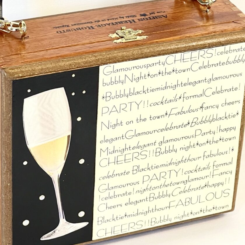 Close-up of an embellished cigar box purse with messages about celebrating and having a glamorous party night, featuring a graphic of a champagne glass.