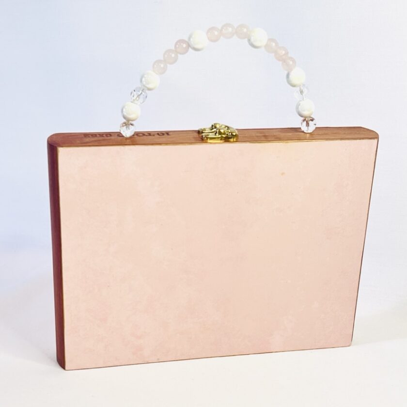 A rectangular pink clutch purse with a pearl handle and gold clasp, displayed against a white background.