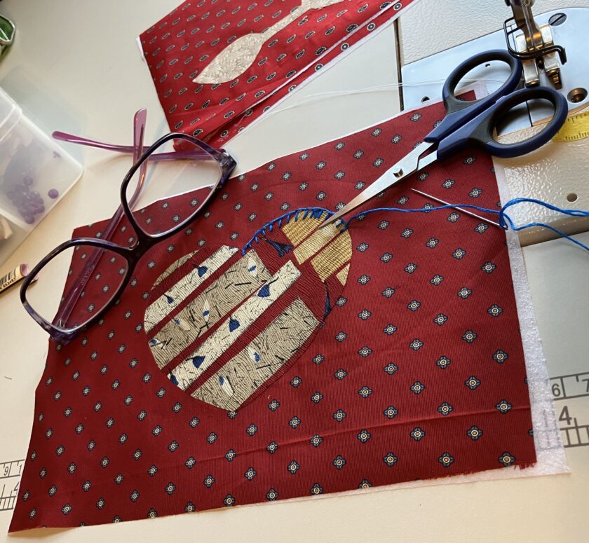Fabric with appliqued hot air balloon design, scissors, and glasses on a sewing table, crafting tools scattered around.