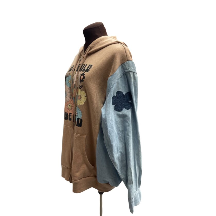 Mannequin displaying a hooded jacket with mixed fabric design, featuring a brown body, blue denim sleeves, and floral embroidery.