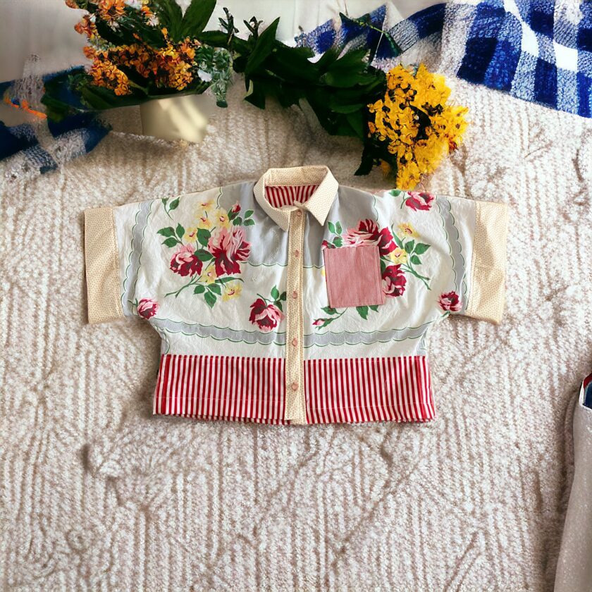 Child's floral jacket with red and white striped sleeves and a pocket, displayed on a textured white blanket, surrounded by colorful flowers.