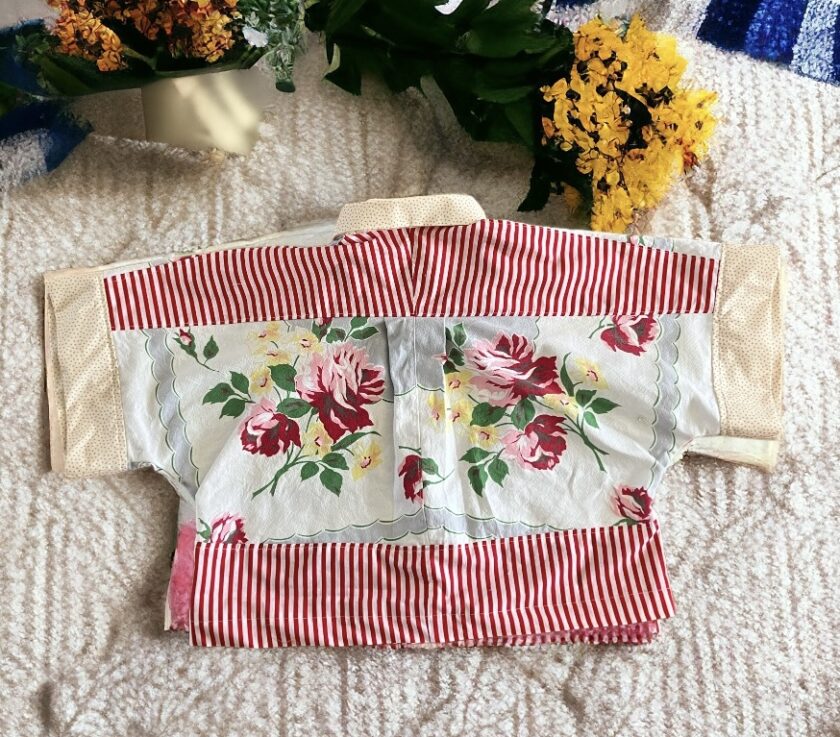 A traditional floral patterned jacket with red and white striped sleeves laid out on a patterned blue and white fabric surface.