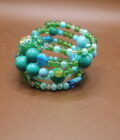 A stack of beaded bracelets in various shades of blue and green on a brown surface.