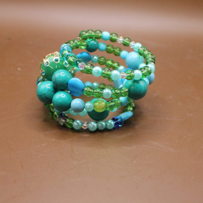 A stack of beaded bracelets in various shades of blue and green on a brown surface.