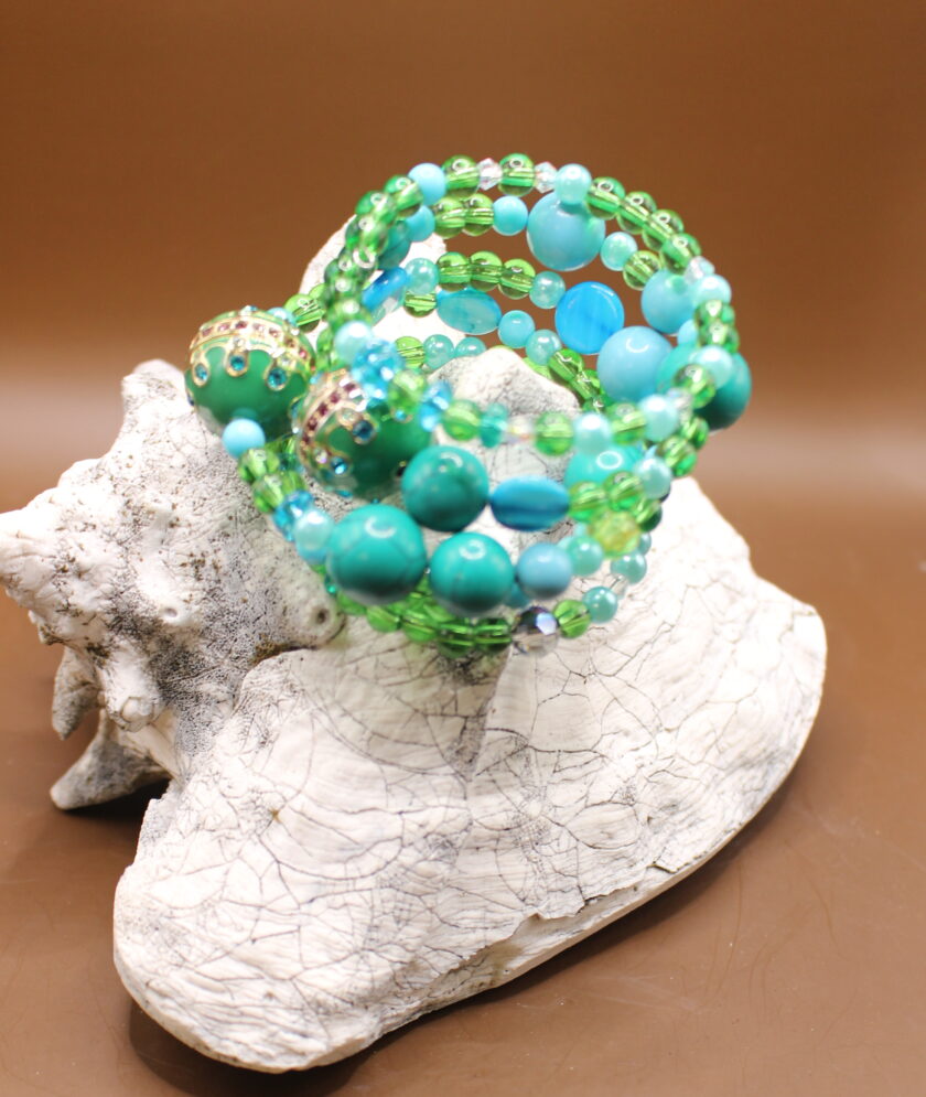 A collection of turquoise and green beaded bracelets displayed on a white, textured stone.