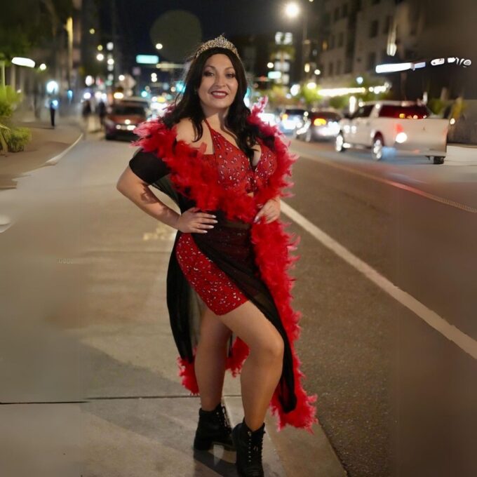 A woman in a red sequined dress and feather boa standing on a city street at night.