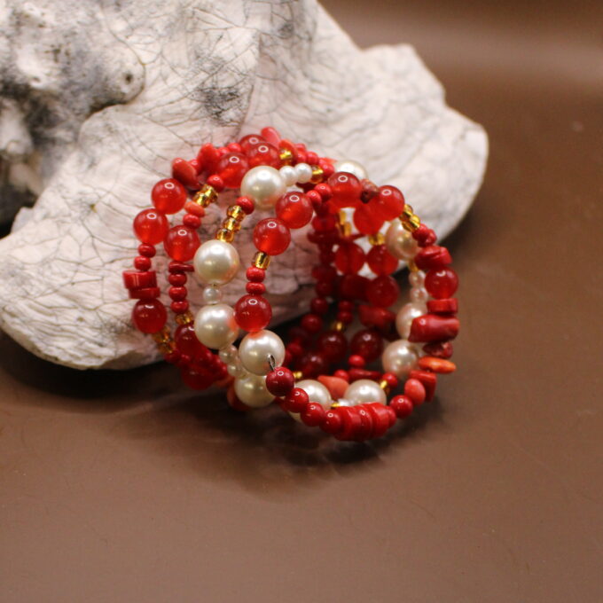 A handcrafted red and white bead bracelet displayed against a stone and brown background.