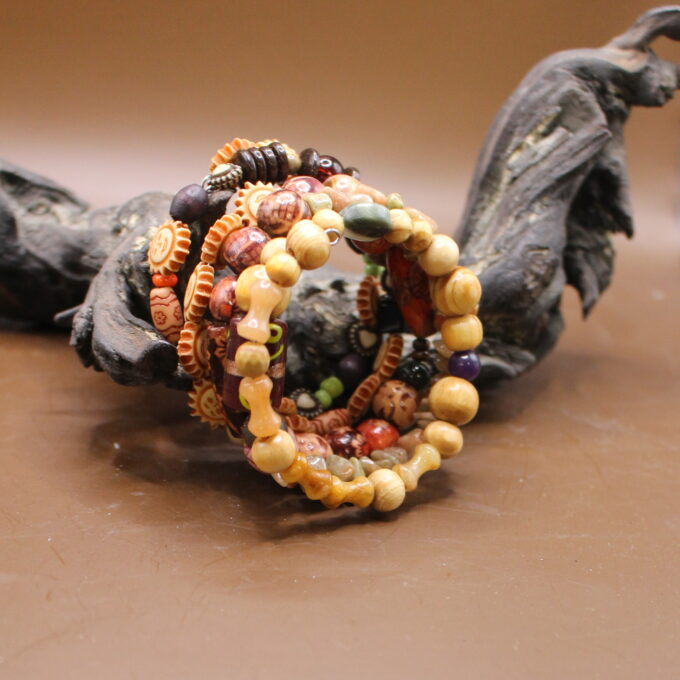A colorful beaded bracelet resting on a wooden surface, with a blurred artistic figurine in the background.