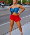 A person in a blue top and red shorts posing on a city street.