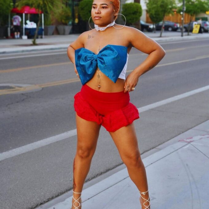 A person in a blue top and red shorts posing on a city street.