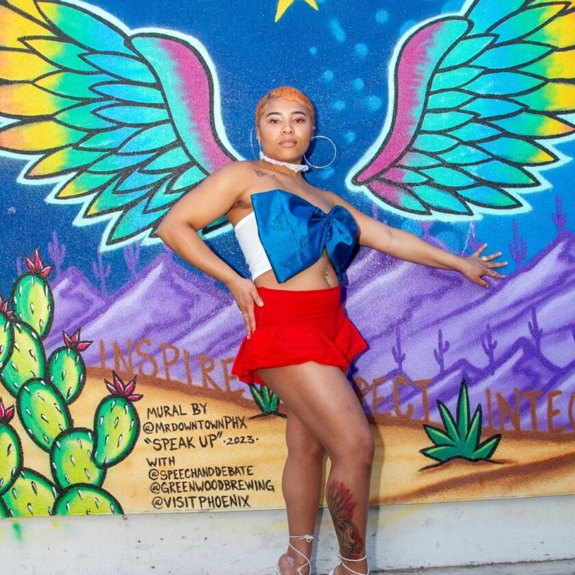 Woman posing in front of a colorful mural with wings.