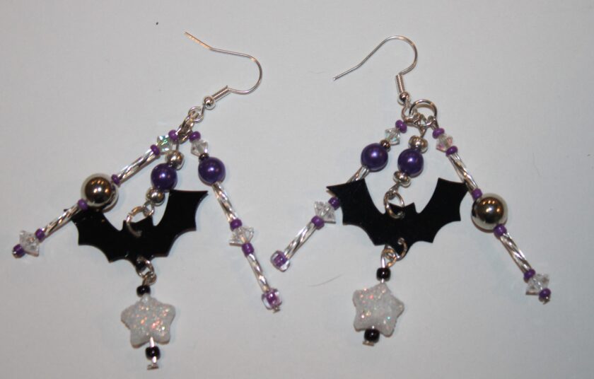 halloween earrings featuring three dangles with purple glass and purple pearls, silver tone and a little black bat in one dangle with a white star